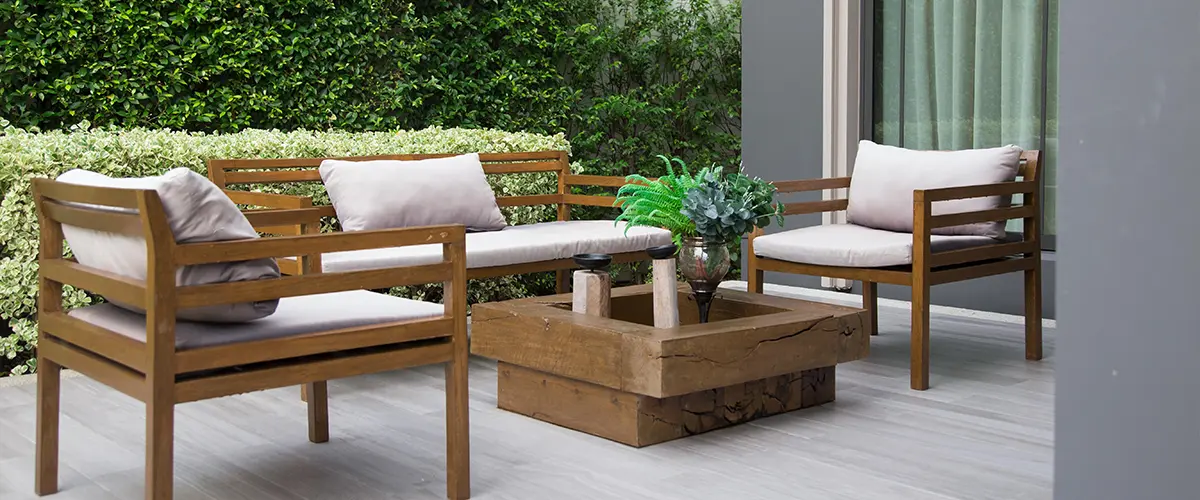 Cozy outdoor patio in Frisco, with outdoor furniture, cushioned seating, a wooden coffee table, and lush green hedges providing a private backdrop.