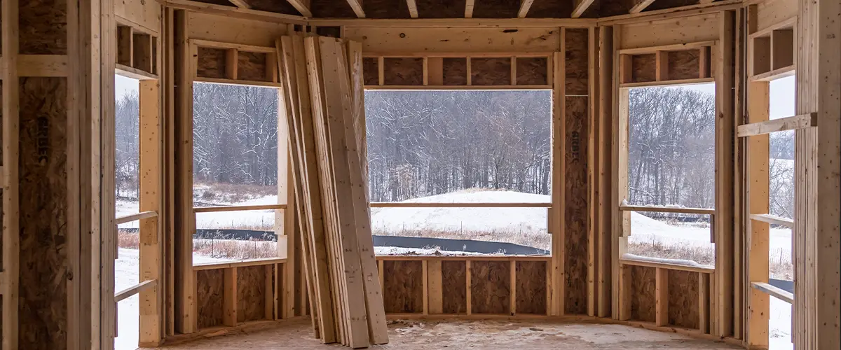 New sunroom construction in Frisco with framed walls, large windows overlooking a snowy landscape, and lumber stacked inside the unfinished room.