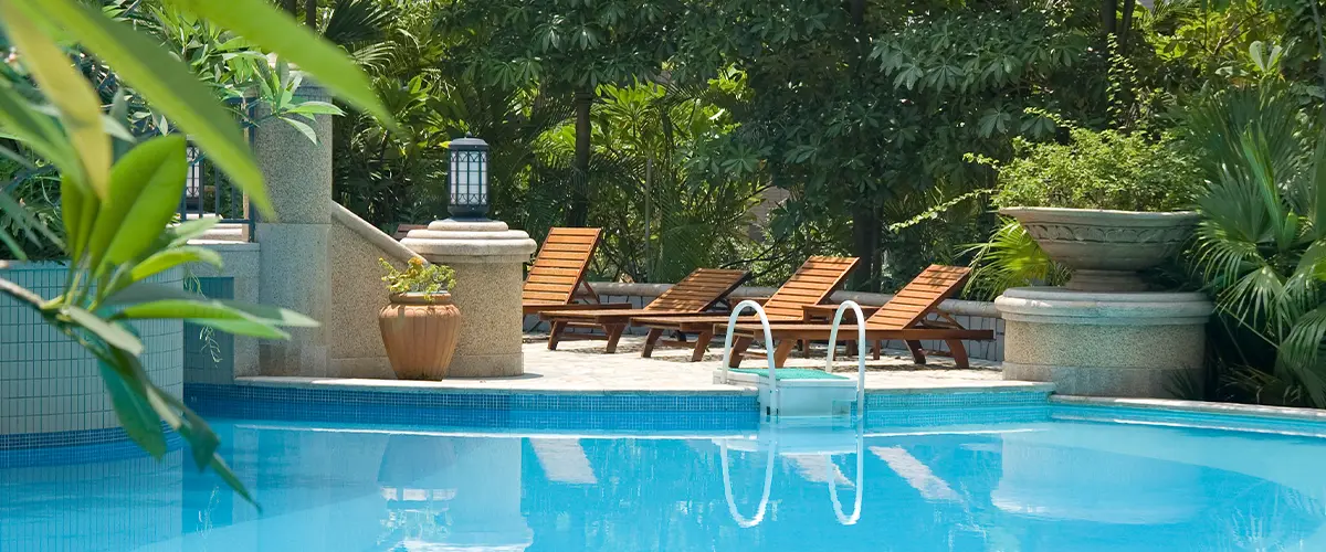 Tropical resort-style pool in Plano, with elegant stone steps, surrounded by lush greenery and wooden lounge chairs.