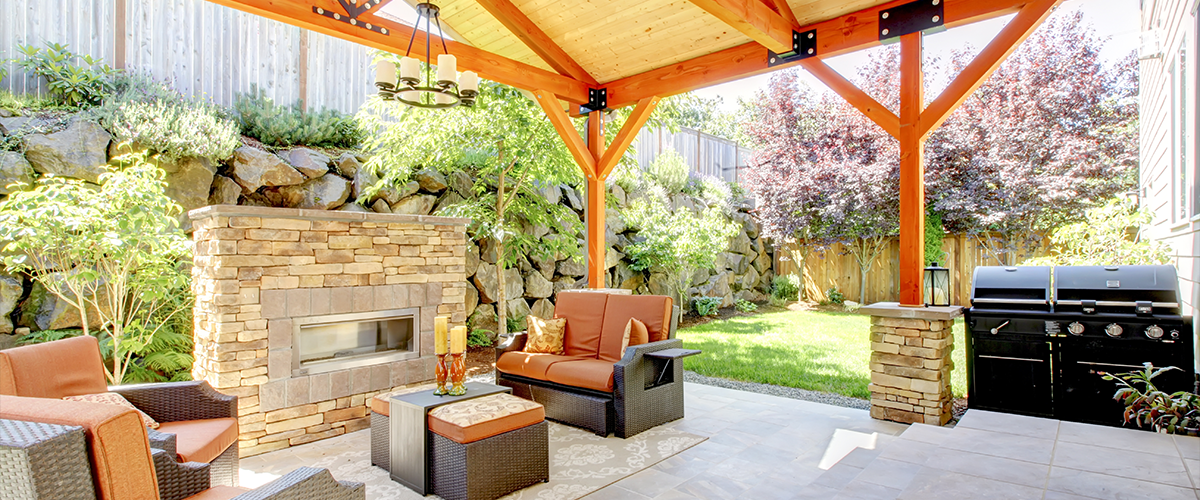 Rustic covered patio with stone fireplace and outdoor grill, ideal for backyard gatherings and cooking.