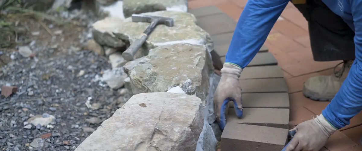 Worker laying bricks for a garden landscape border, creating a natural and structured outdoor space.