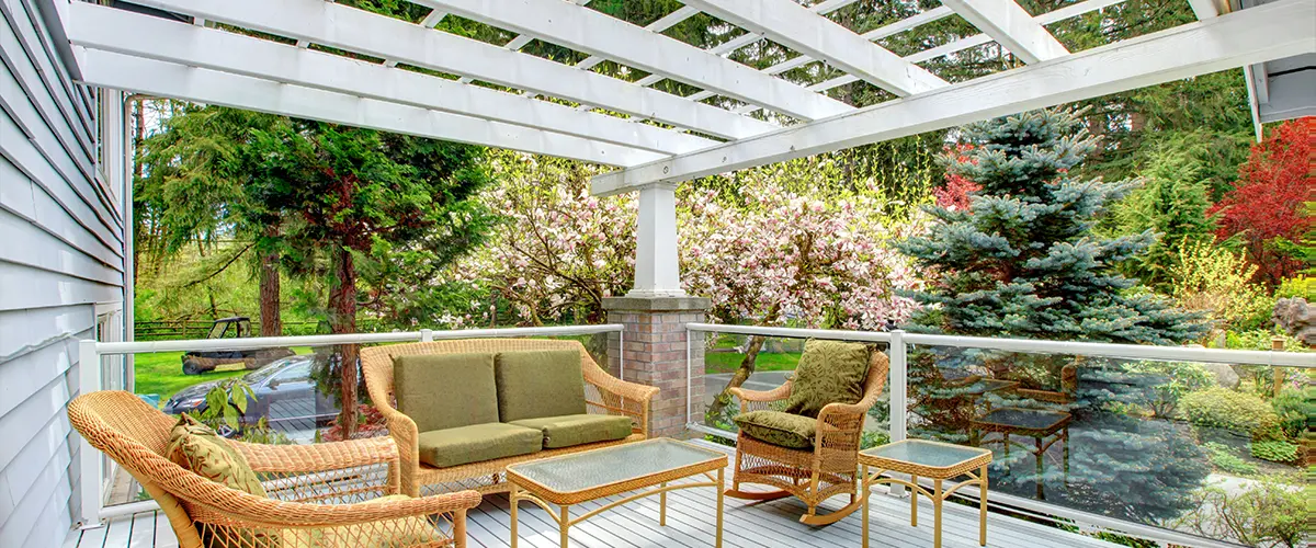 Covered patio with wicker furniture and garden view, featuring a white pergola and spring blossoms