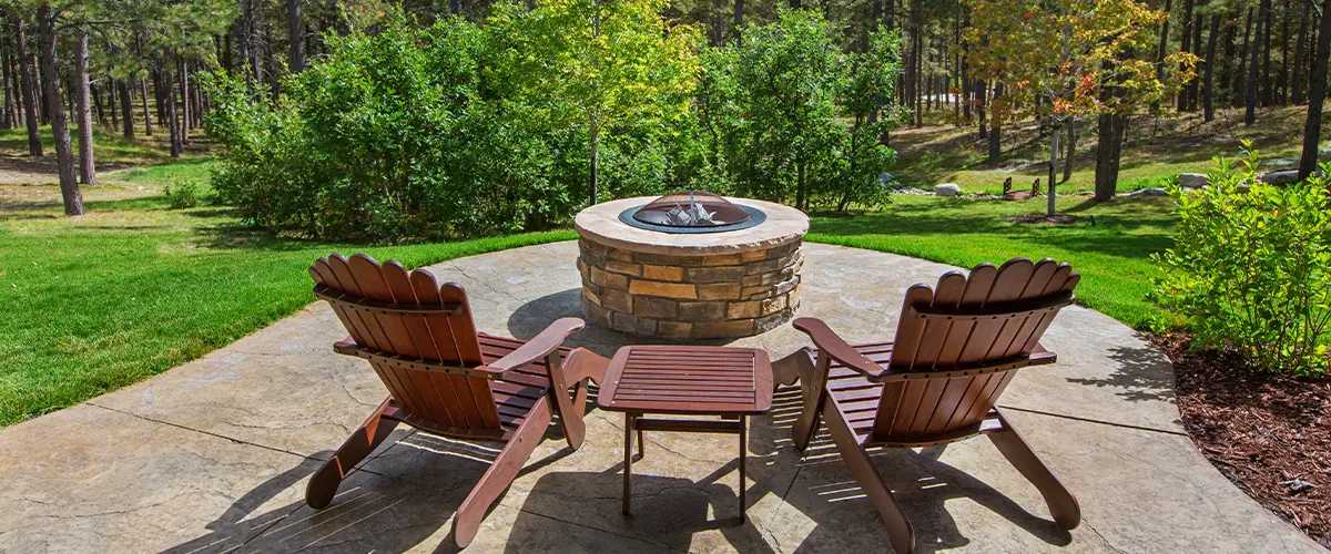 Outdoor deck with wooden Adirondack chairs surrounding a stone fire pit in a forest setting