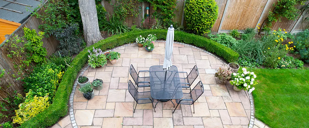 Top-down view of a landscaped patio with stone tiles, black metal dining furniture, lush greenery, and garden beds.