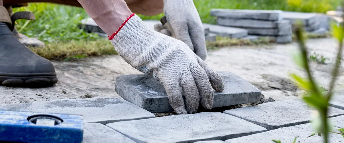 Worker laying gray stone pavers on a garden pathway.