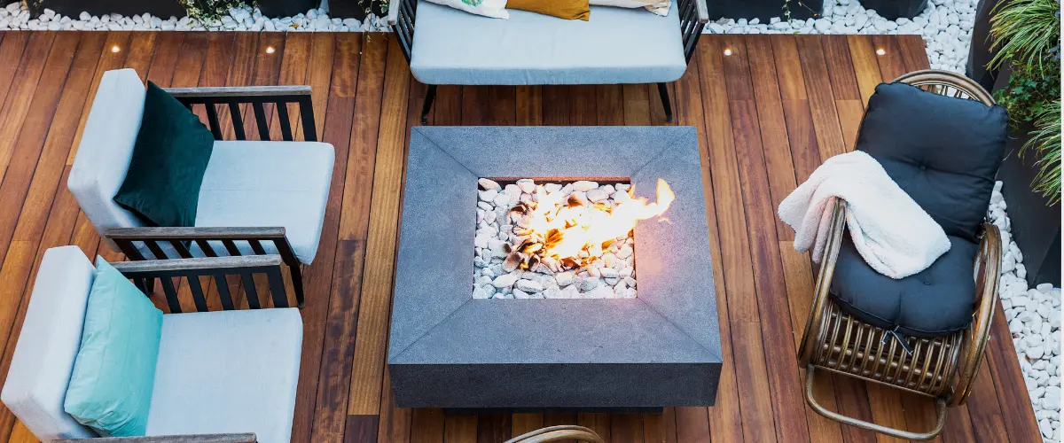 A modern wooden deck with a fire pit, surrounded by stylish seating and white stone landscaping