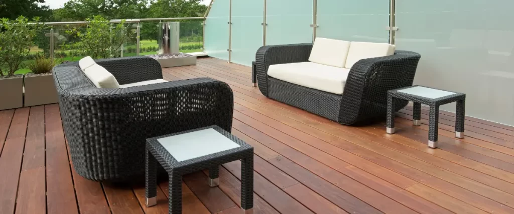 A modern wooden deck with dark wicker furniture and a glass railing, overlooking a green landscape