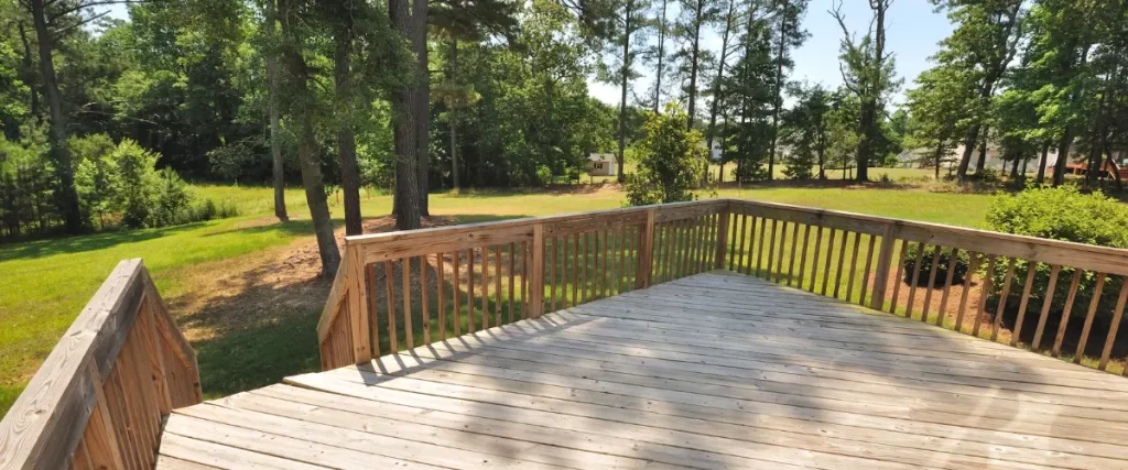 A spacious wooden deck with a simple railing, overlooking a large backyard with trees and greenery